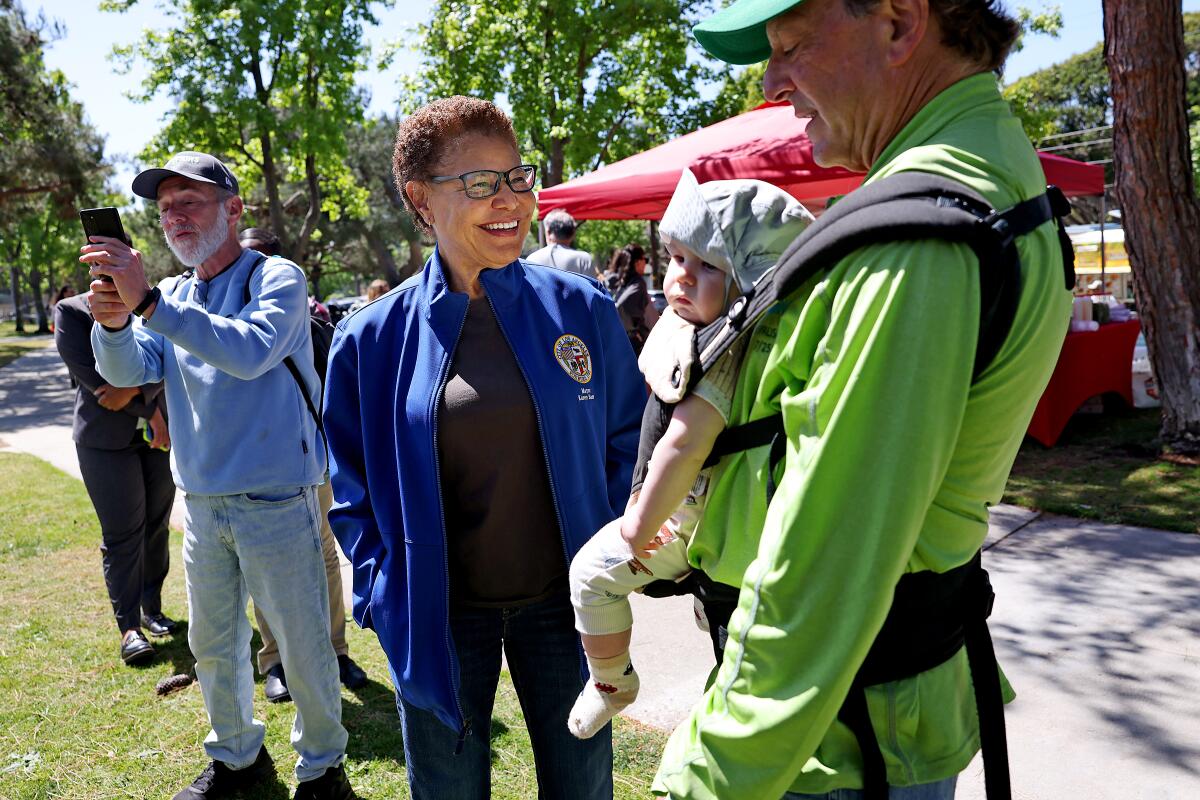 Mayor Karen Bass, center, chats with a resident holding a baby in a carrier