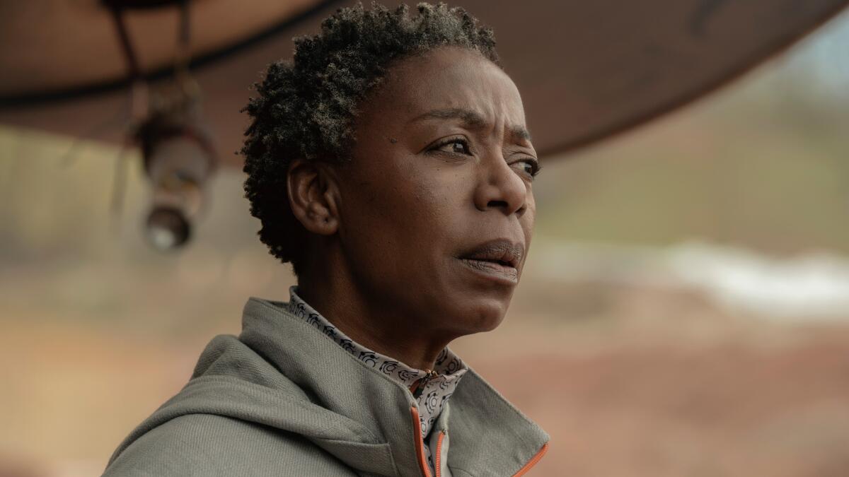 Dr. Mensah (Noma Dumezweni), a frowning woman with short gray hair, stands outside.