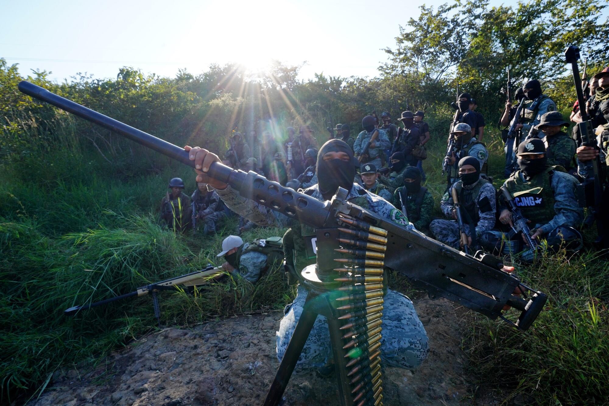 Troops in combat fatigues and balaclavas pose with a machine gun and other large arms in a rural area