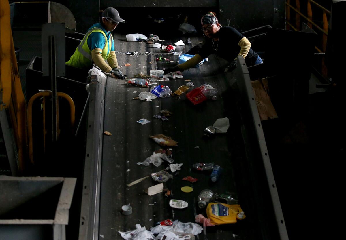Workers sort through recyclable plastic waste traveling on a conveyor belt.