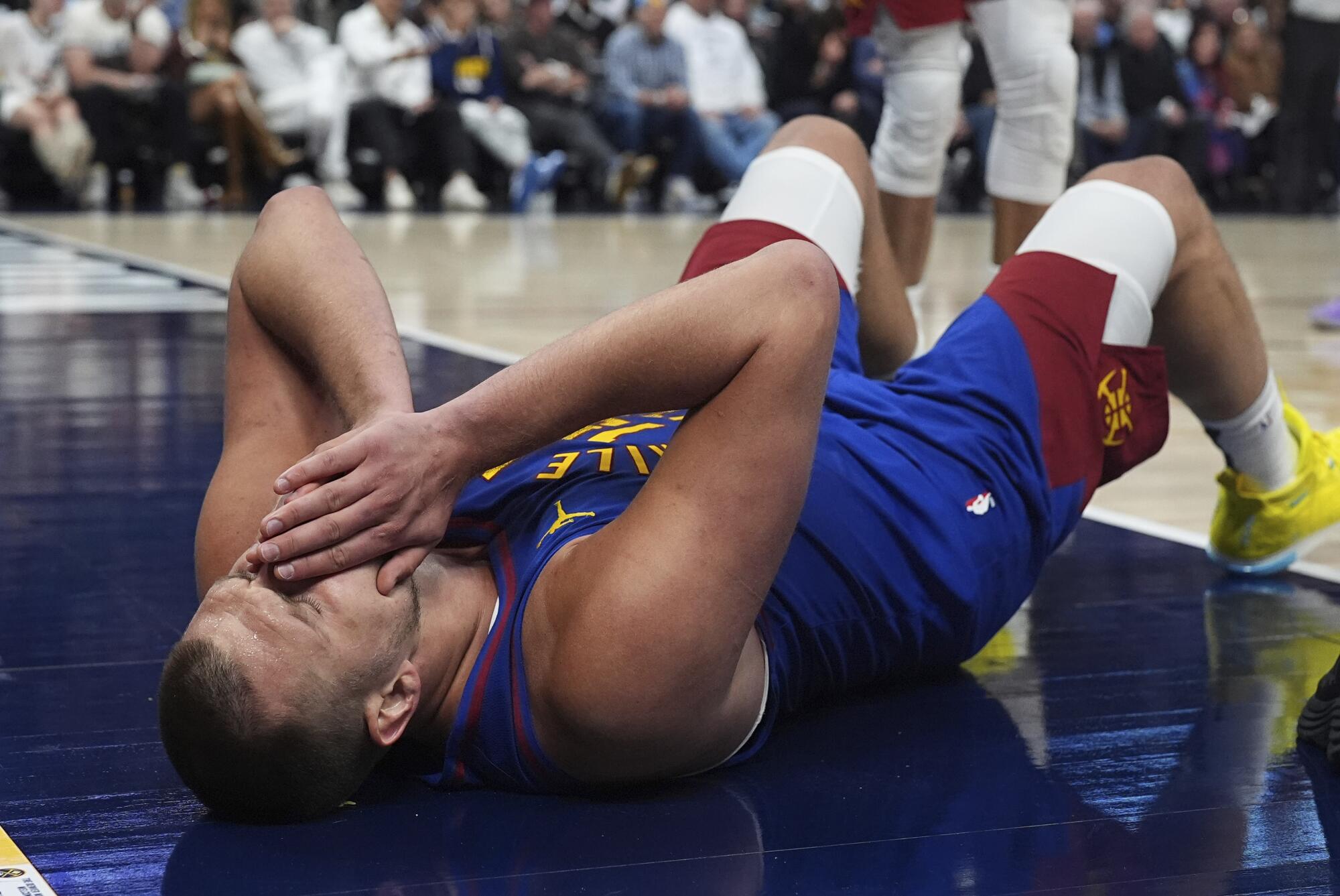 Nuggets center Nikola Jokic lays on the court and holds his nose after taking a hit to the face during a playoff game