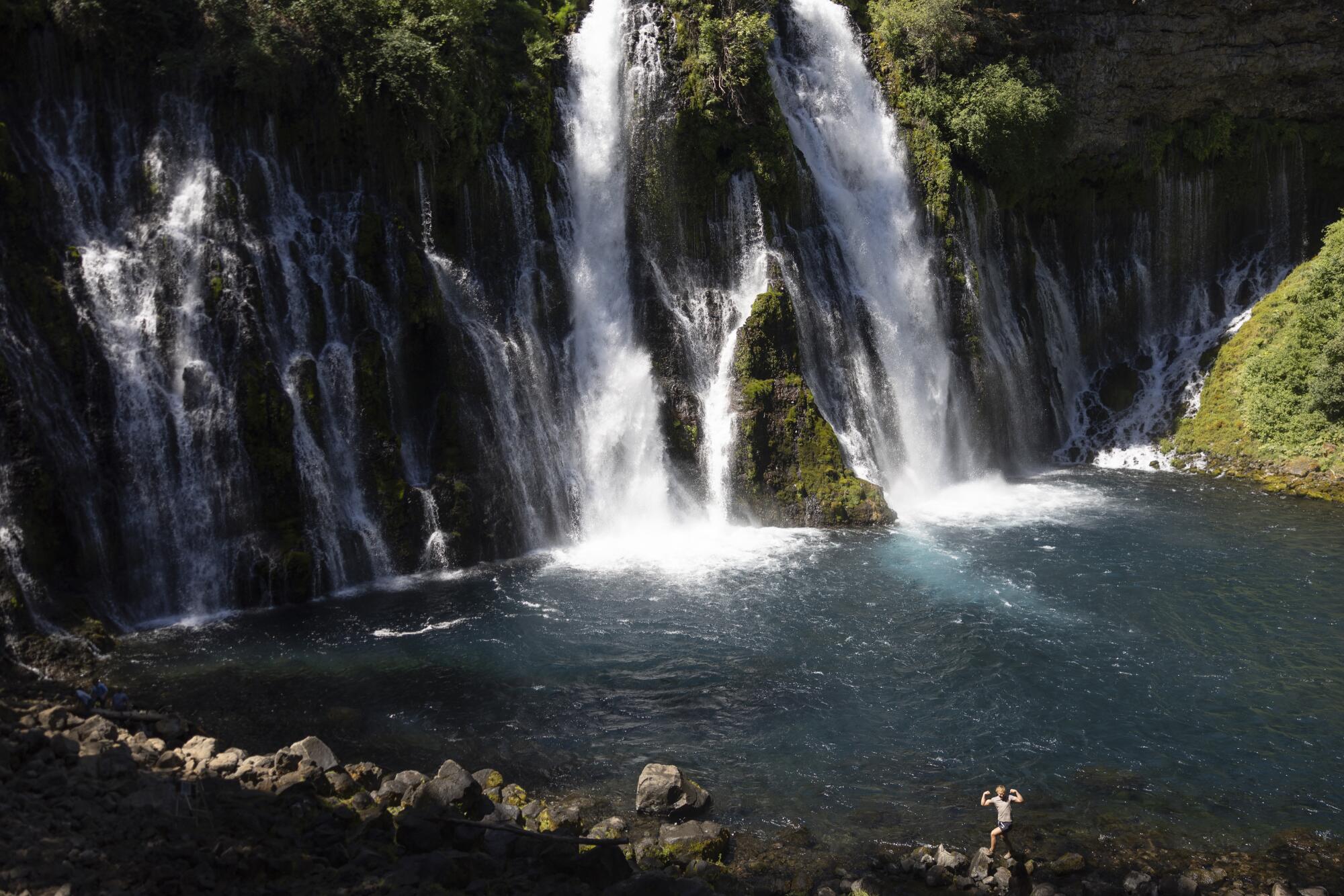 A visitor poses with arms raised on a rock at Burney Falls.