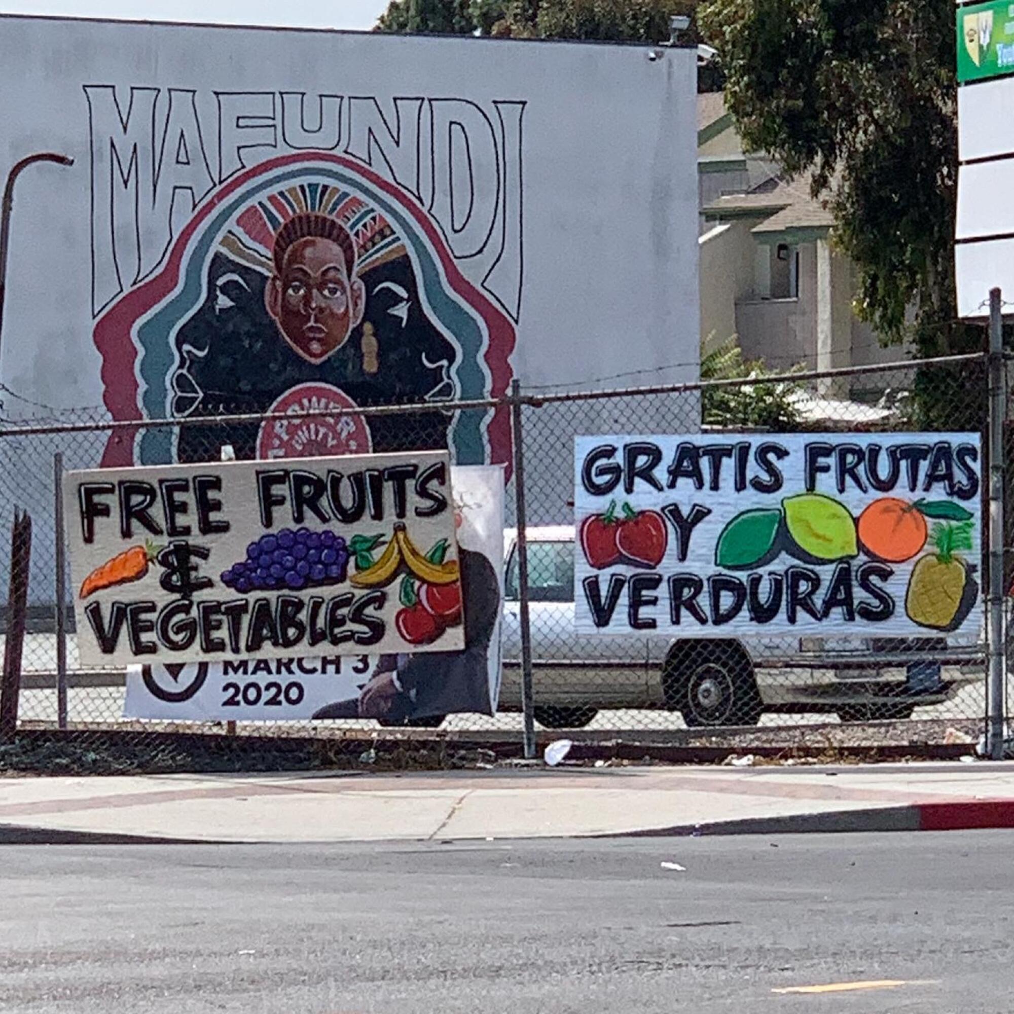 Signs outside of a parking lot promoting free fruits and vegetables in English and Spanish