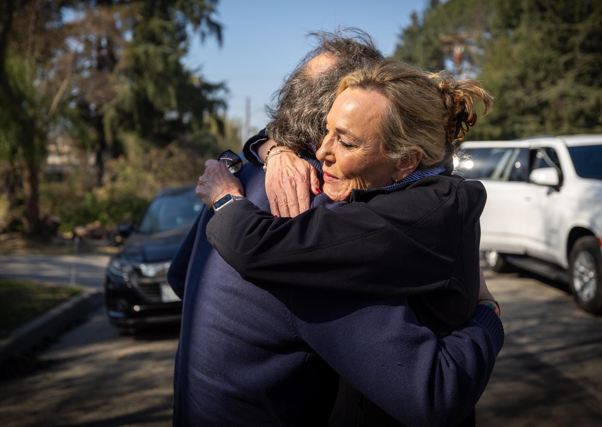 A man and a woman hug on a tree-lined street.